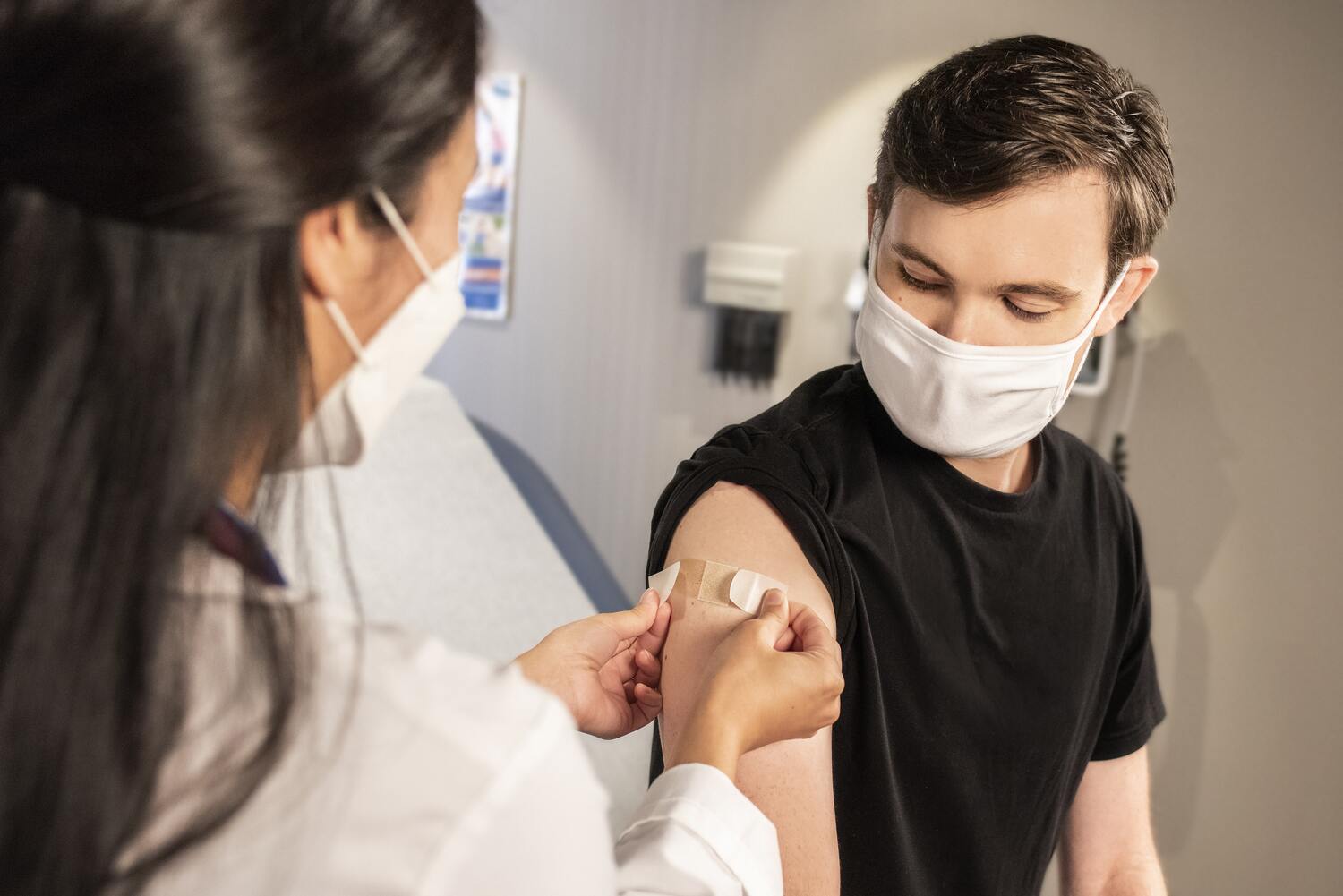 Un professionnel de santé fait une piqure dans le bras d'un patients. Ils sont masqués